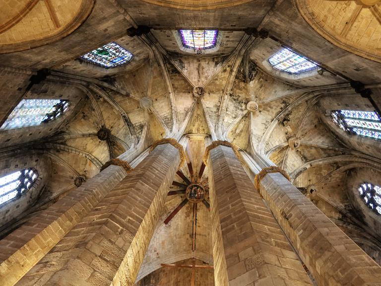 Blick in ein altes, sehr hohes Kirchen-Deckengewölbe mit bunten Glasfenstern.