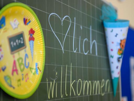 An einer Tafel im Klassenzimmer steht "Herzlich Willkommen", daneben hängt eine Schultüte.