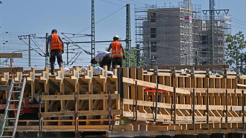 Arbeiter auf einer Baustelle mit Gerüsten vor einem eingerüsteten Gebäude in Erfurt 