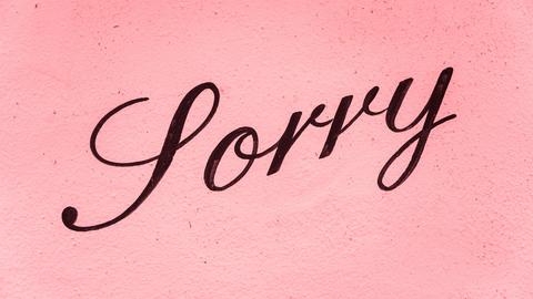 Auf einer rosafarbenen Wand steht in schwarzer Schrift "Sorry".