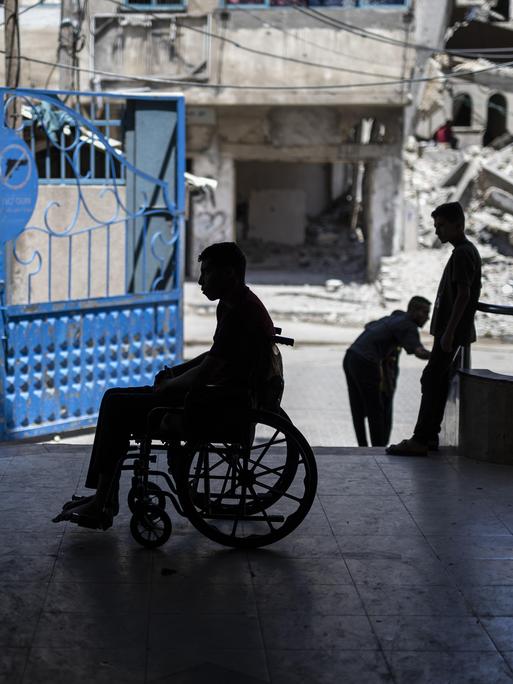 Ein Mann in einem Rollstuhl, im Hintergrund sind Trümmer von Gaza-Stadt zu sehen