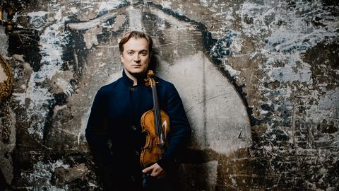 Capuçon steht in dunklem Konzert-Outfit vor einer Wand voller Graffiti.