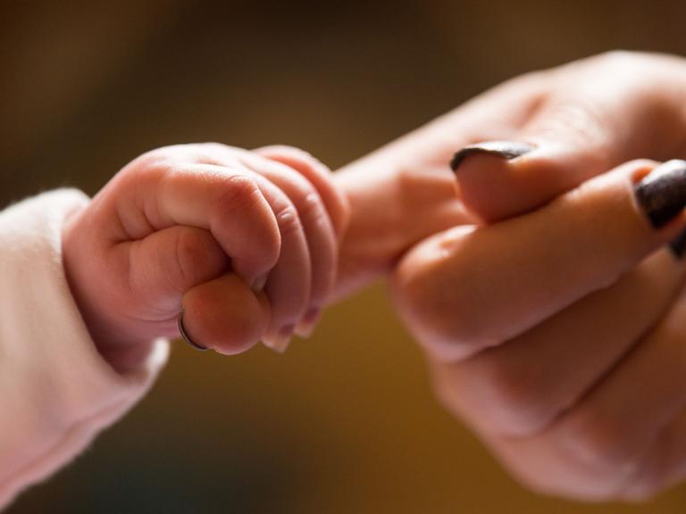 Eine Hand eines Babys greift den Zeigefinger eines Erwachsenen. 