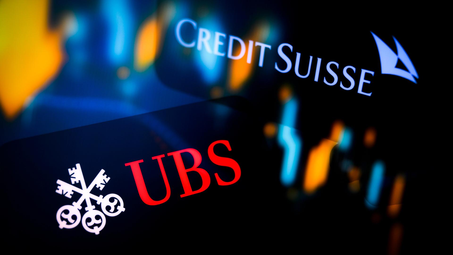 Leuchtende Logos der Banken UBS und Credit Suisse auf dunklem Hintergrund