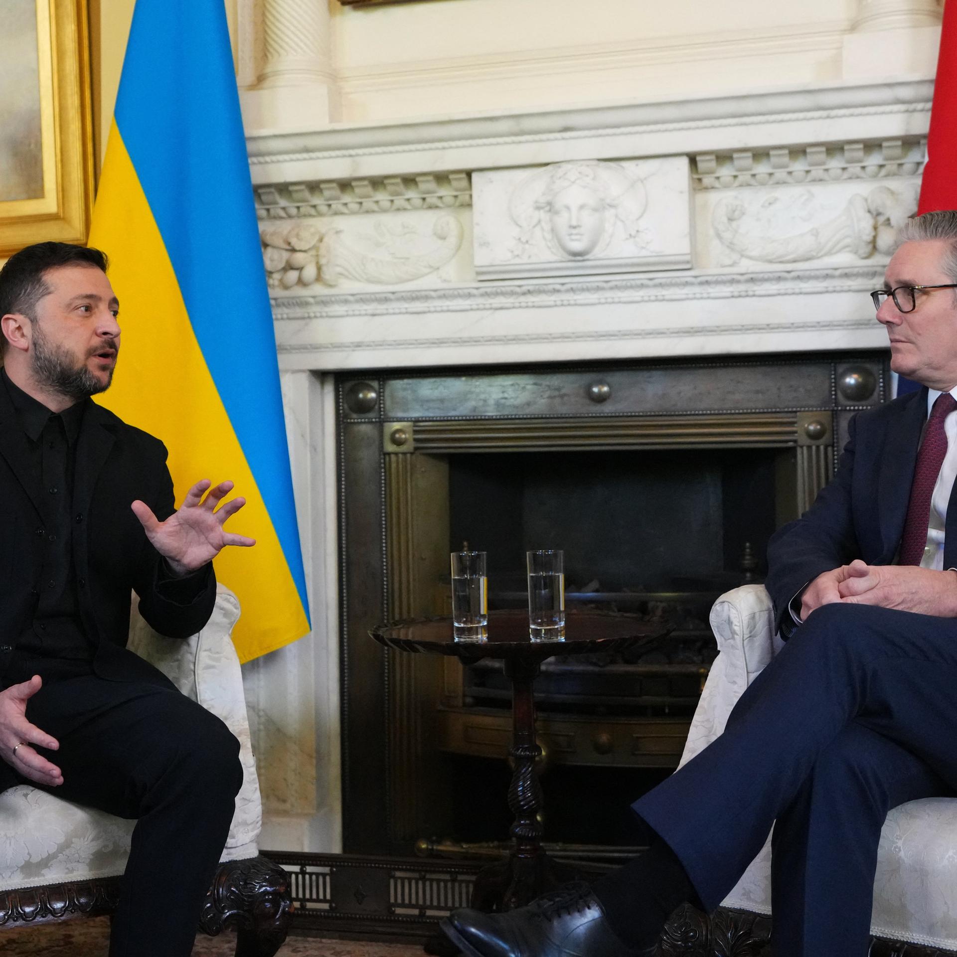 Der ukrainische Präsident Wolodymyr Selensykj (l.) und der britische Premierminister Keir Starmer (r.) sitzen nebeneinander, hinter ihnen die Nationalflaggen. Selenskyj spricht und gestikuliert.