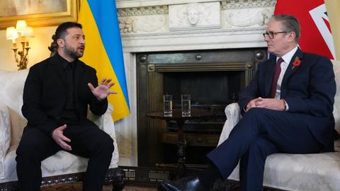 Der ukrainische Präsident Wolodymyr Selensykj (l.) und der britische Premierminister Keir Starmer (r.) sitzen nebeneinander, hinter ihnen die Nationalflaggen. Selenskyj spricht und gestikuliert.