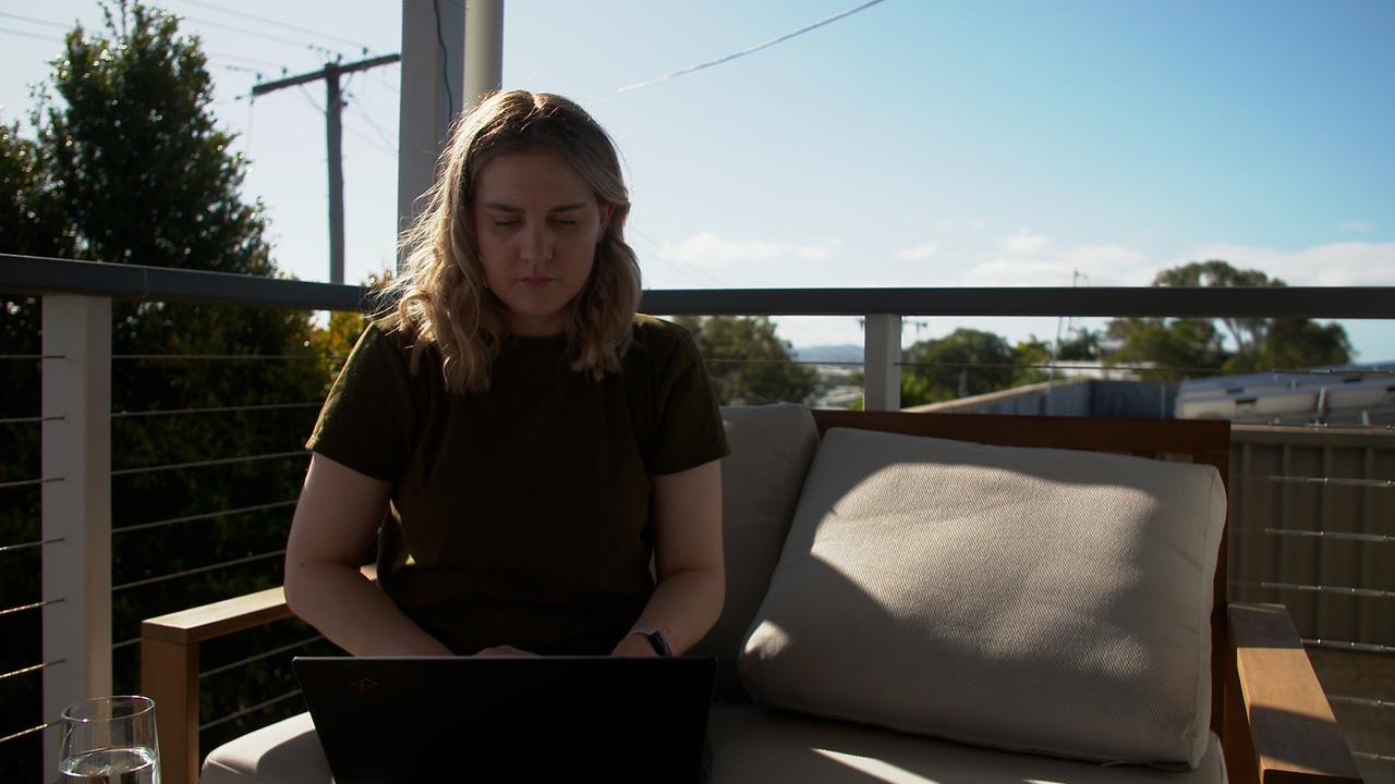Eine junge blonde Frau sitzt unter blauem Himmel auf einer Couch auf einer Dachterrasse.