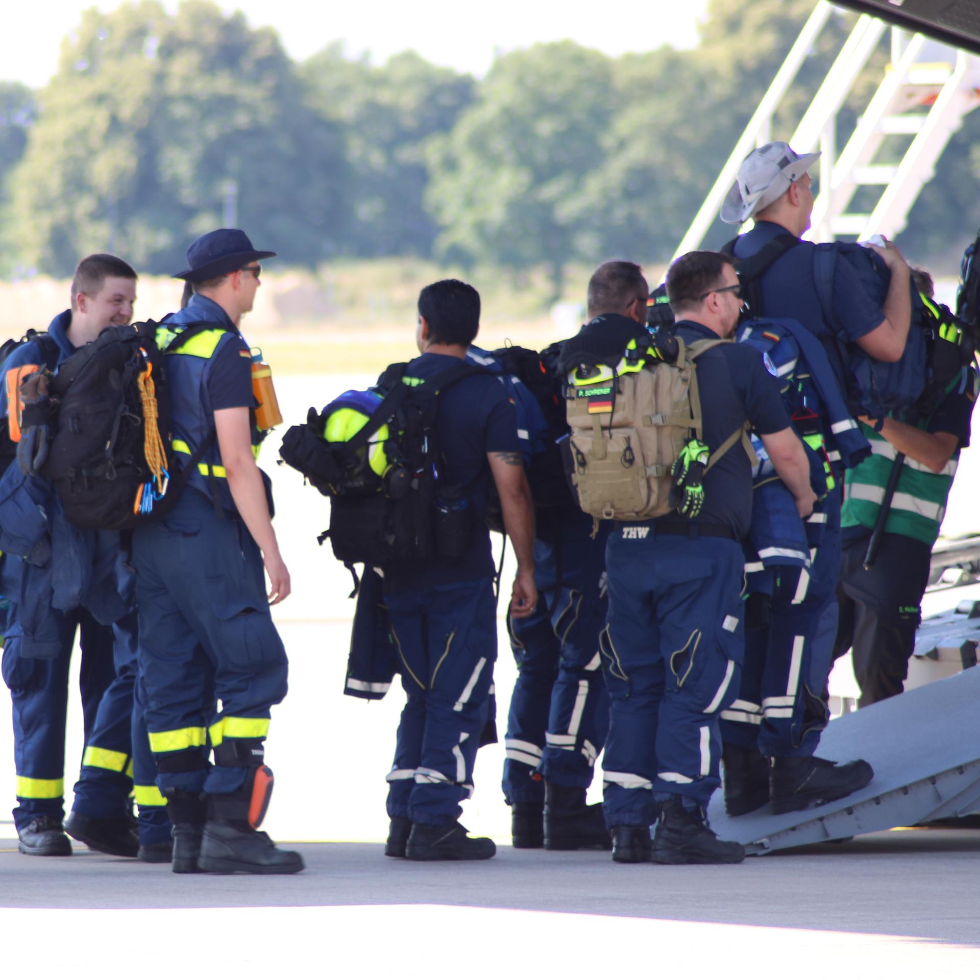 Einsatzkräfte in Arbeitskleidung stehen vor einem Flugzeug in einer Reihe.