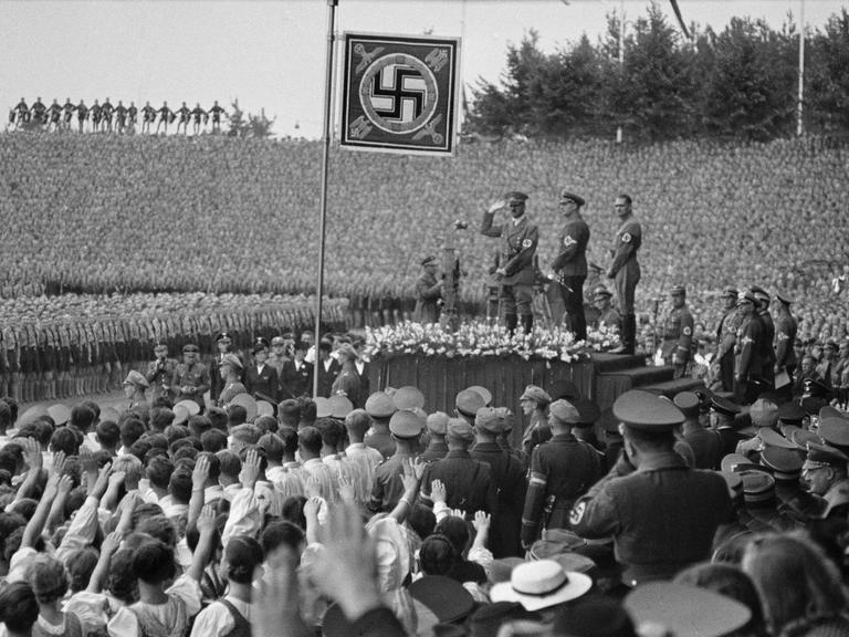 Historische Aufnahme vom Aufmarsch beim 10. Reichsparteitag der NSDAP im Stadion von Nürnberg am 10. September 1938: Hitler mit dem Reichsjugendführer Baldur von Schirach und Rudolf Heß auf der Tribüne. 