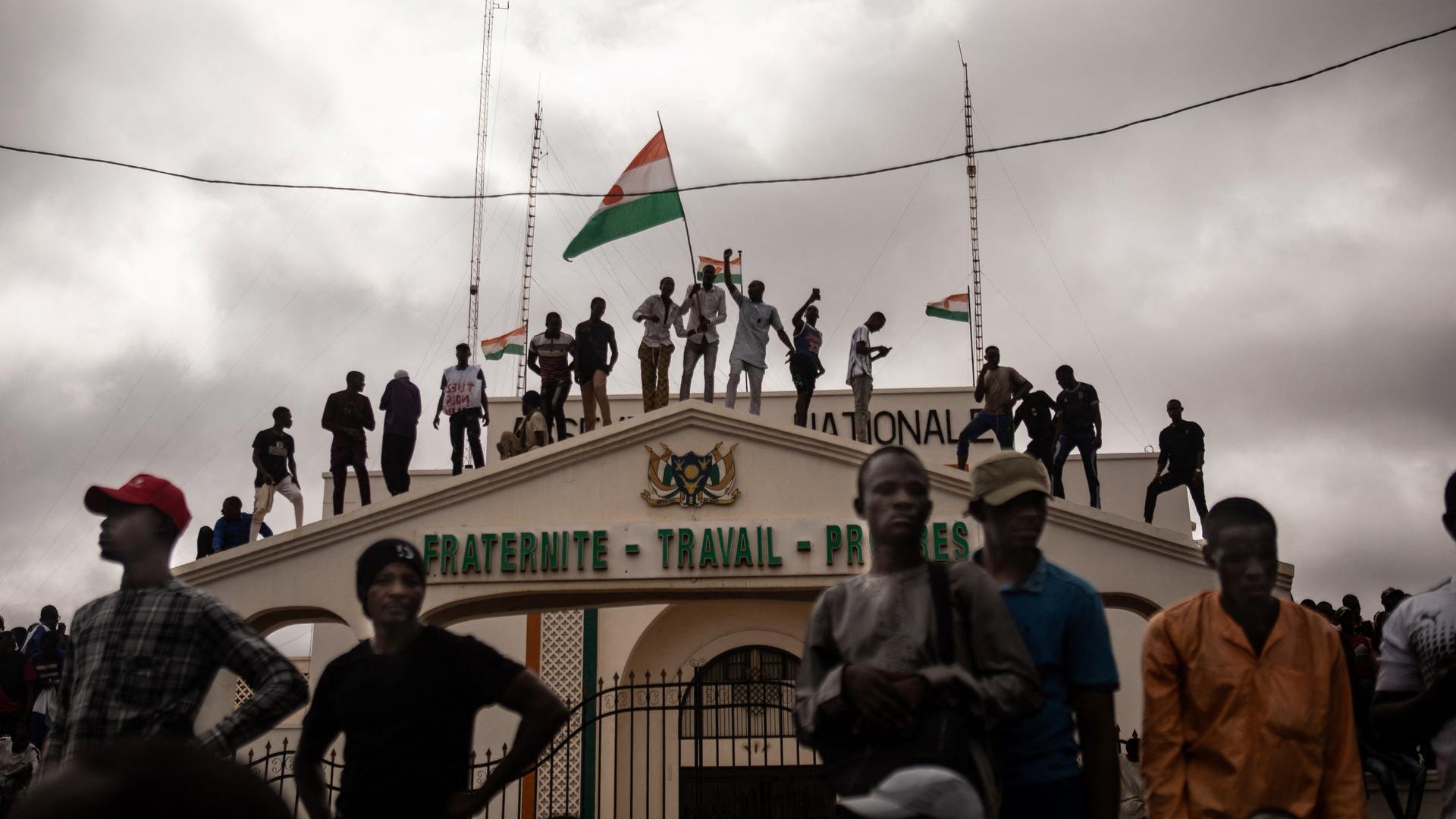 Menschen stehen auf dem Dach eines Gebäudes in Niamey und schwenken die nigrische Flagge.