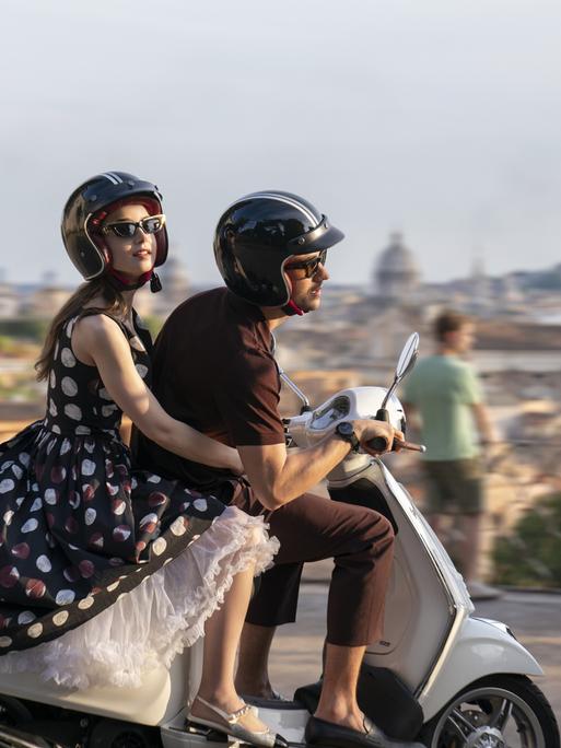 Die Schauspieler Lily Collins und Eugenio Franceschini sitzen auf einem Motorroller und fahren durch Rom. 