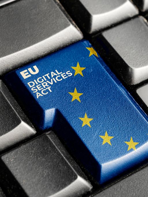 Fotografie einer schwarzen Computertastatur, mit einer blauen Enter-Taste, auf der die Europa-Flagge und der Schriftzug "Digital Services Act" zu sehen sind.