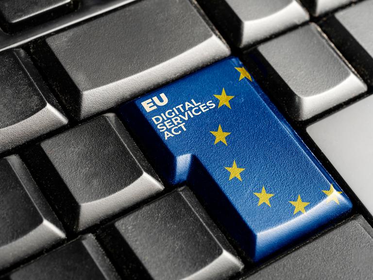 Fotografie einer schwarzen Computertastatur, mit einer blauen Enter-Taste, auf der die Europa-Flagge und der Schriftzug "Digital Services Act" zu sehen sind.
