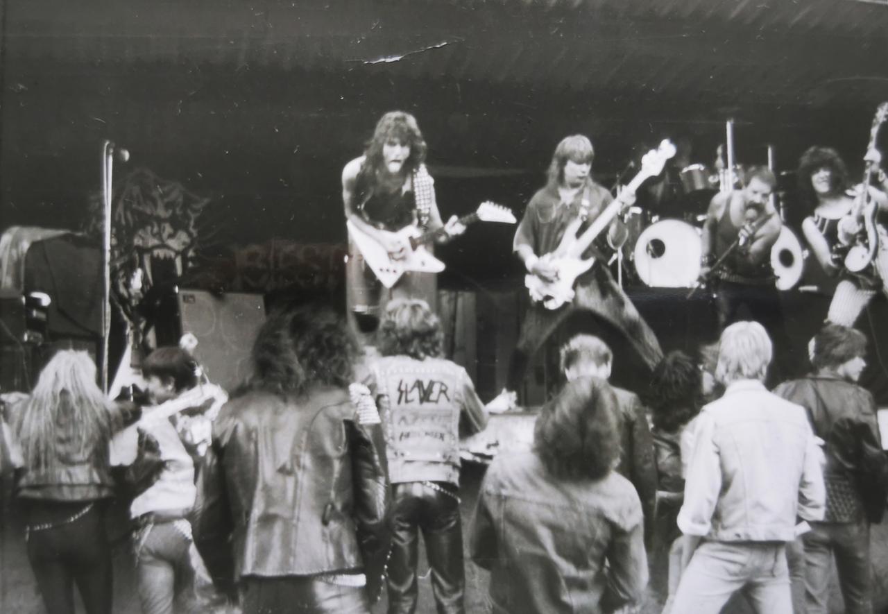 Schwarzweißfoto von einem Auftritt der Band Biest. Vor der Bühne steht Publikum in Jeans, Lederhosen und Kutten.