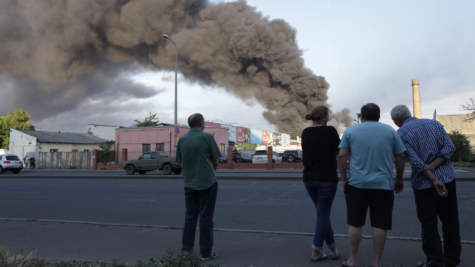 Menschen stehen in Odessa in der Ost-Ukraine auf der Straße. Im Hintergrund ist eine große Rauchwolke zu sehen. 