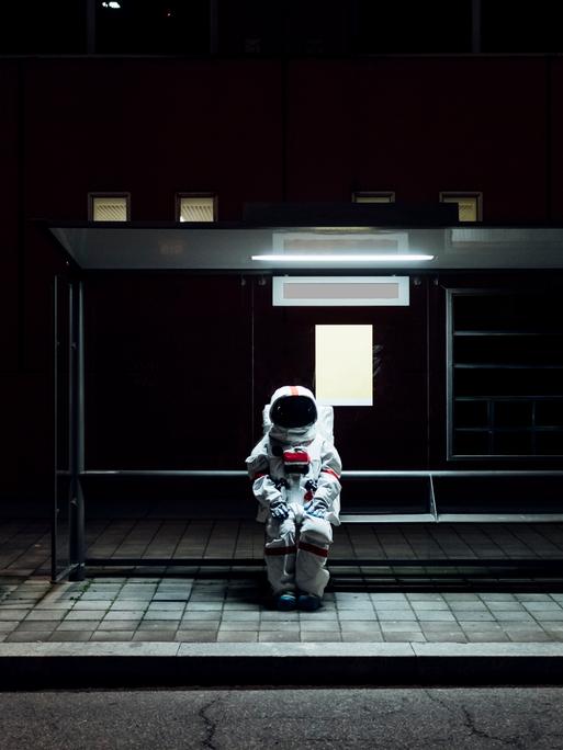 Ein Astronaut sitzt allein im Dunkeln an einer Bushaltestelle.