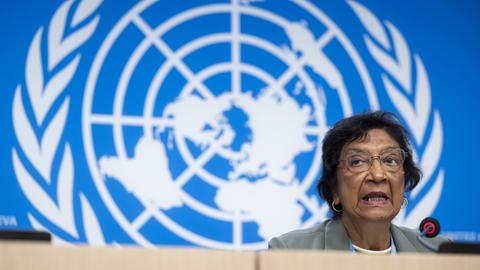 Navi Pillay spricht während einer Pressekonferenz in ein Mikro, im Hintergrund sieht man das Logo der United Nations