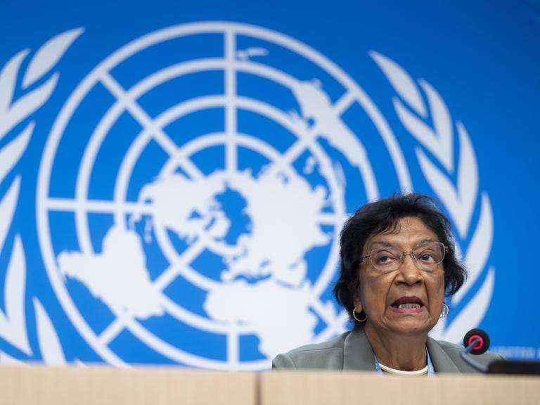 Navi Pillay spricht während einer Pressekonferenz in ein Mikro, im Hintergrund sieht man das Logo der United Nations