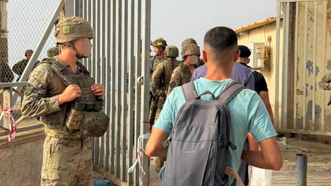 Mehrere Menschen gehen durch ein großes Tor, daneben stehen Soldaten.