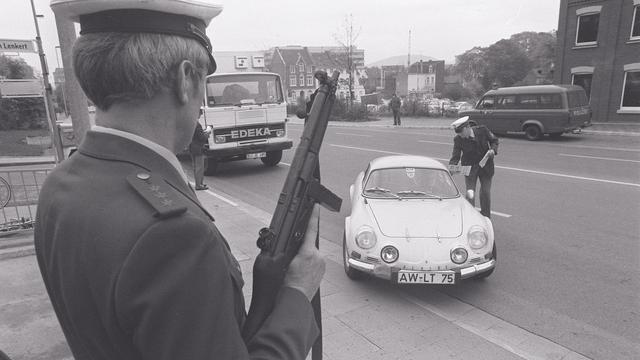 Eine Polizeikontrolle in den 70er-Jahren. Ein Polizist posiert mit einem Maschinengewehr. Ein anderer Polizist verteilt Flugblätter an die Insassen eines angehaltenen Autos.