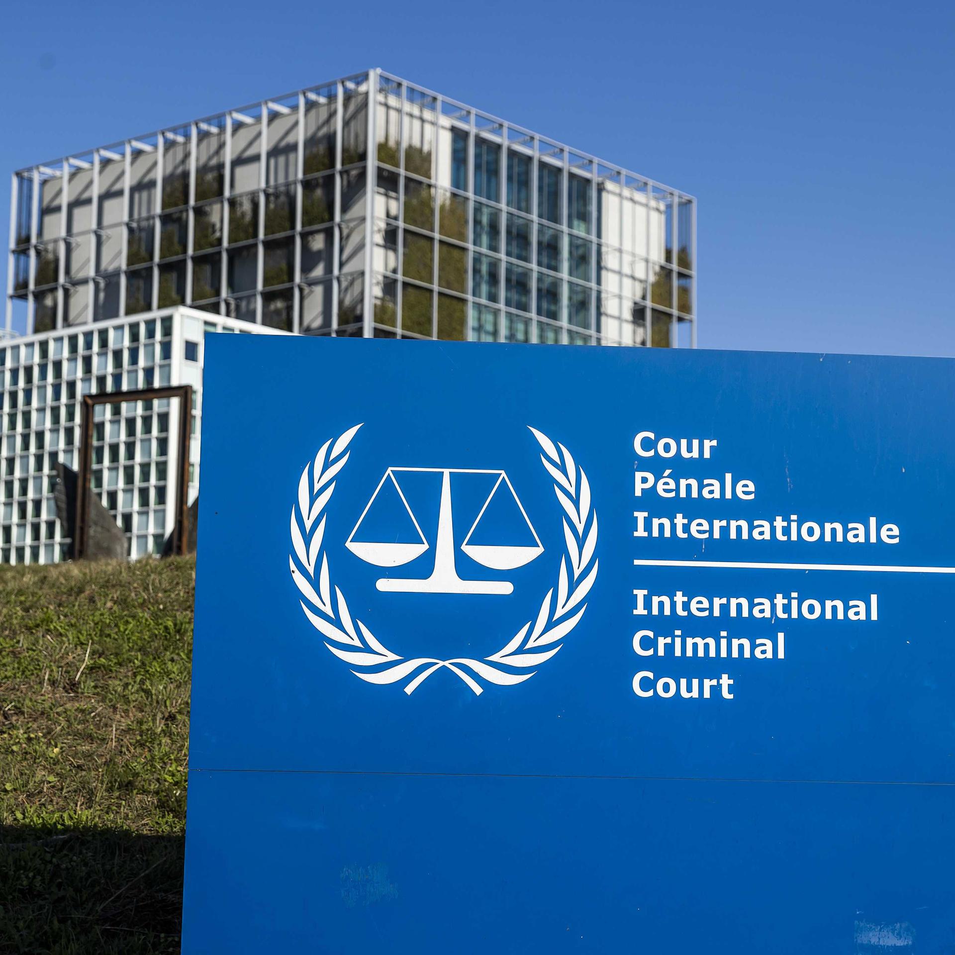 Im Hintergrund ein Gebäude, davor ein blaues Schild mit der weißen Aufschrift "International Criminal Court".