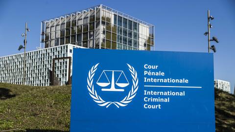 Im Hintergrund ein Gebäude, davor ein blaues Schild mit der weißen Aufschrift "International Criminal Court"