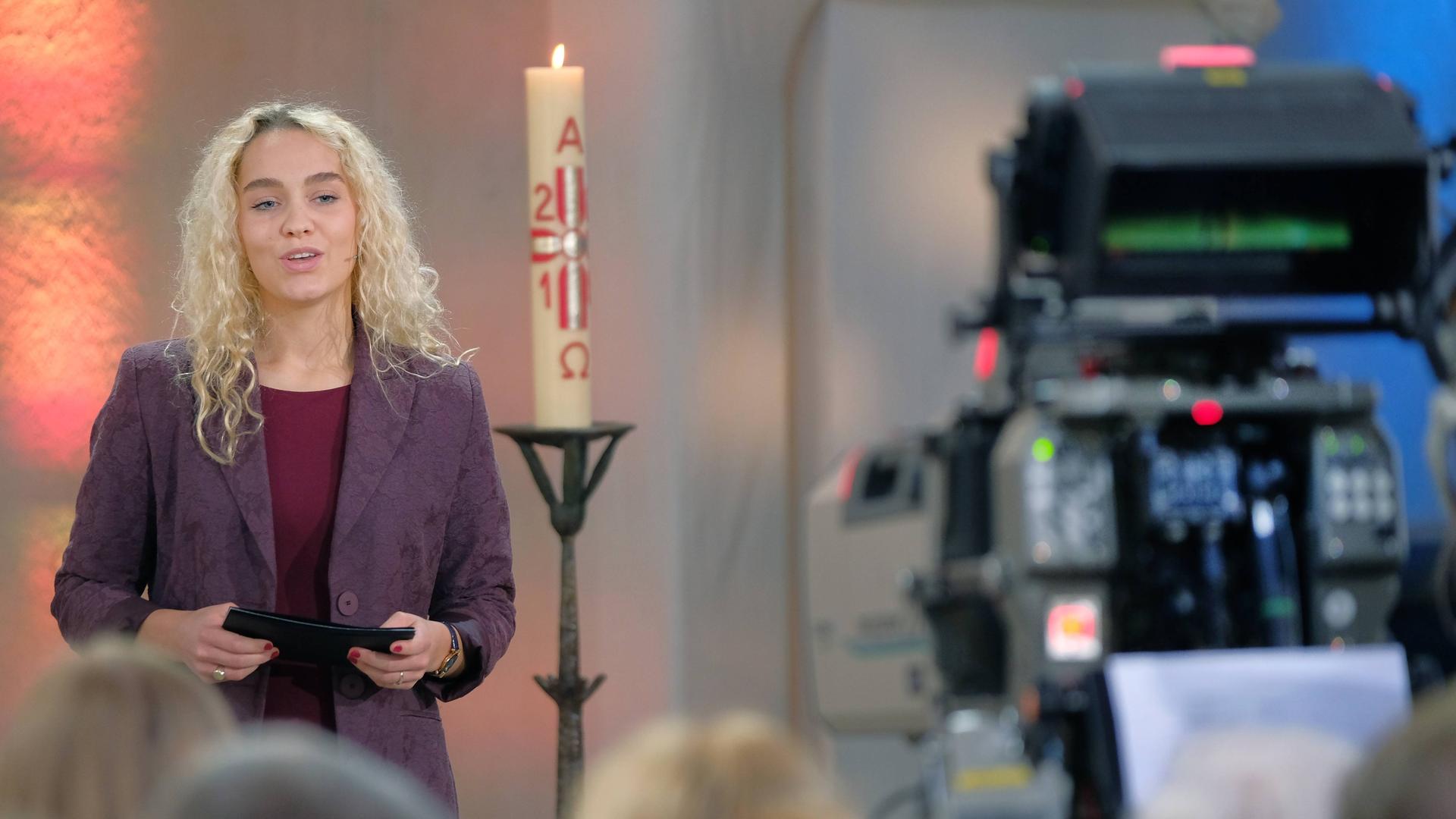 Jana Highholder steht in einer Kirche neben einer Kerze