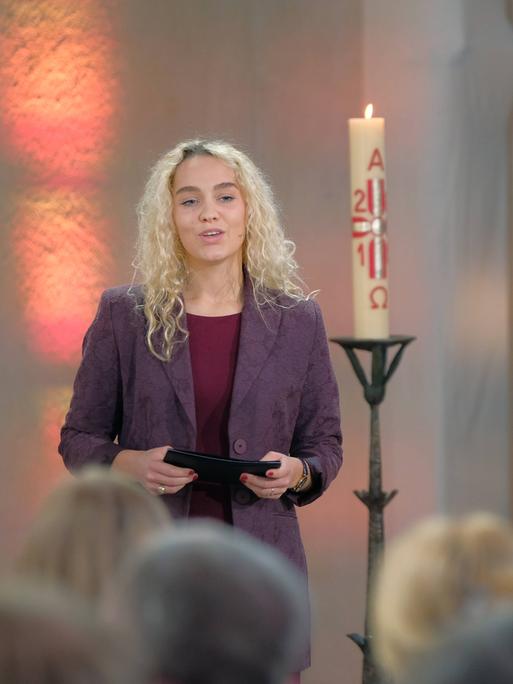 Jana Highholder steht in einer Kirche neben einer Kerze