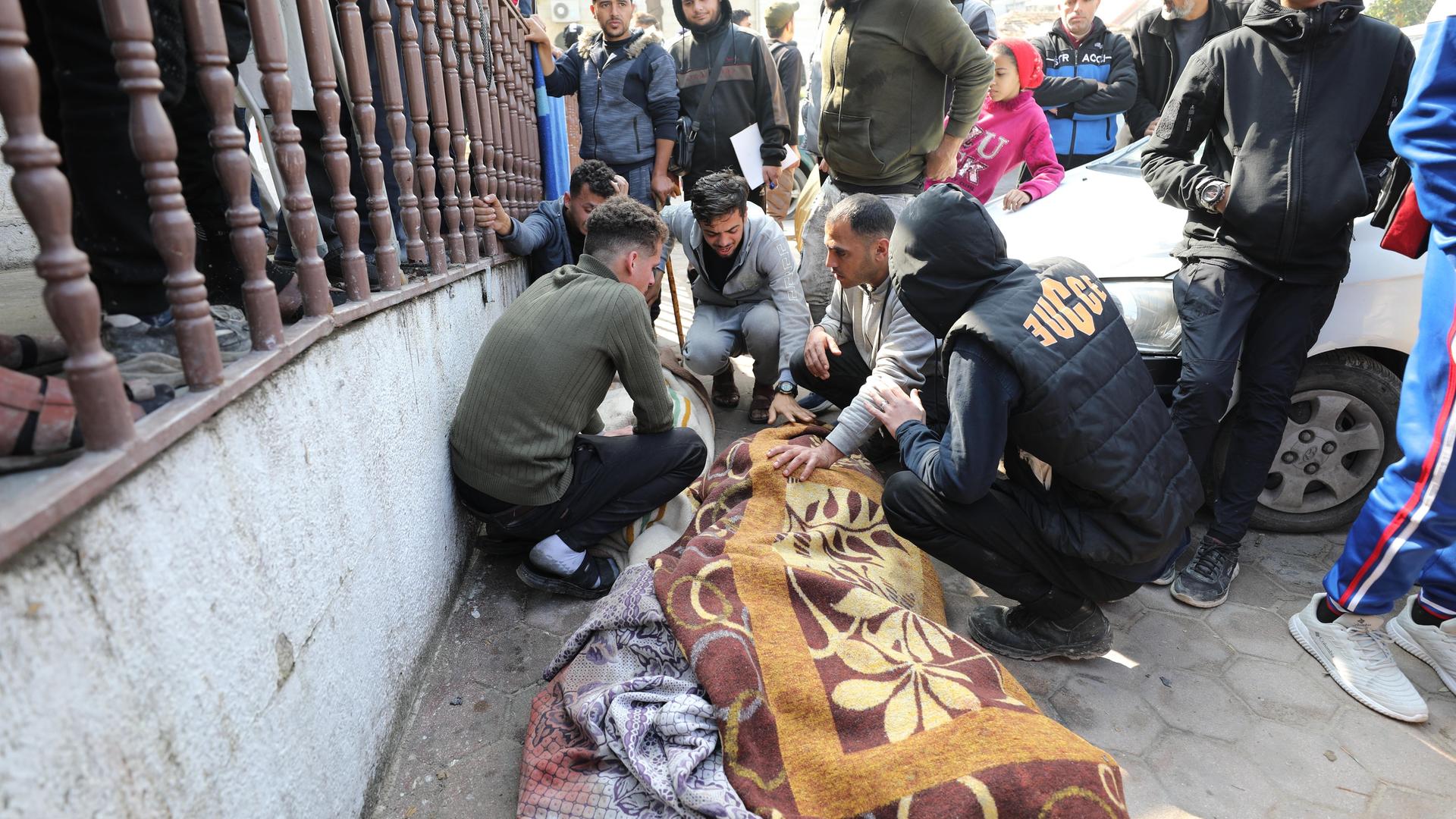 Mehrere Männer in Gaza kauern vor einer mit einer Decke verdeckten Leiche. 