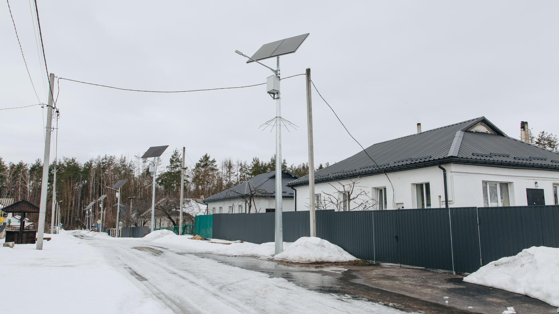 Blick in eine verschneite Straße mit Einfamilienhäusern. An den Strommasten sind Solarpaneele installiert.