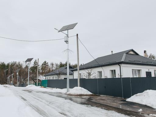Blick in eine verschneite Straße mit Einfamilienhäusern. An den Strommasten sind Solarpaneele installiert.