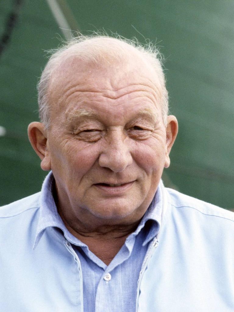 Der Schriftsteller James Krüss 1988. Er steht vor einem Schiff mit dunkelgrünem Anstrich und lächelt verschmitzt. 