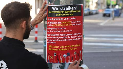 Ein Mann bringt ein Plakat zum Streikaufruf an. Die Überschrift lautet "Wir streiken! Wir protestieren gegen Faschismus und Rassismus!"