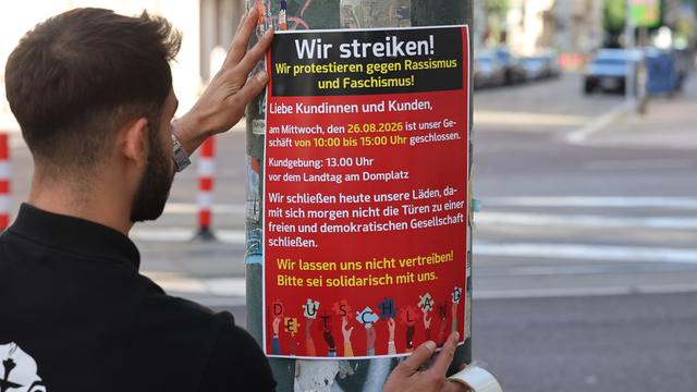 Ein Mann bringt ein Plakat zum Streikaufruf an. Die Überschrift lautet "Wir streiken! Wir protestieren gegen Faschismus und Rassismus!" Ein Mann bringt ein Plakat zum Streikaufruf an. Die Überschrift lautet "Wir streiken! Wir protestieren gegen Faschismus und Rassismus!"