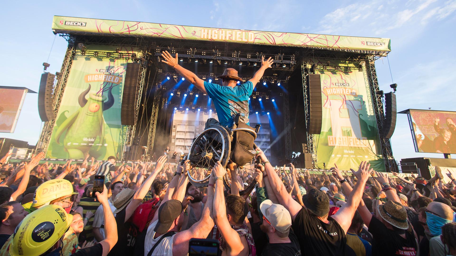 Bei einem Rockkonzert wird ein Rollstuhlfahrer mit seinem Rollstuhl vom Publikum nach oben gehoben, so dass er über den Köpfen zu schweben scheint.