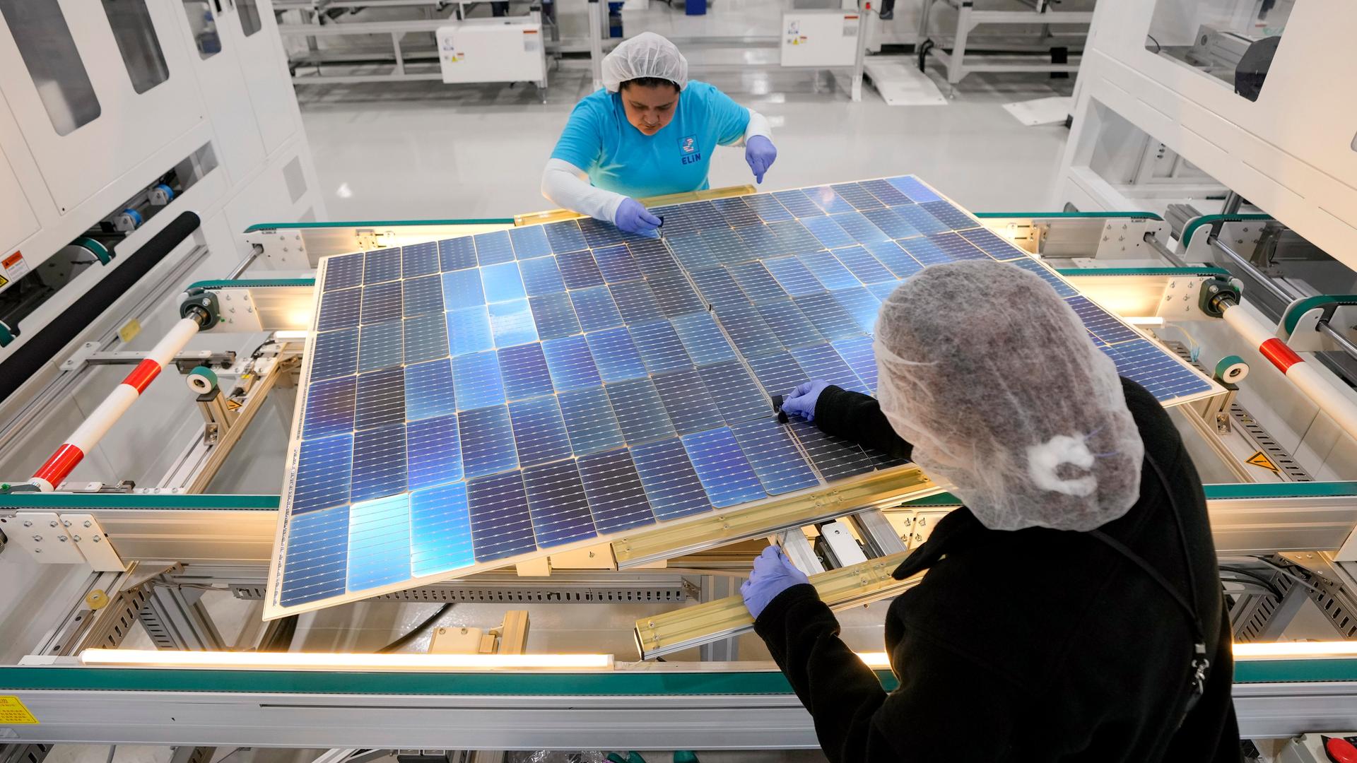 Zwei Frauen arbeiten in einer Fabrik an Solarpaneelen. 