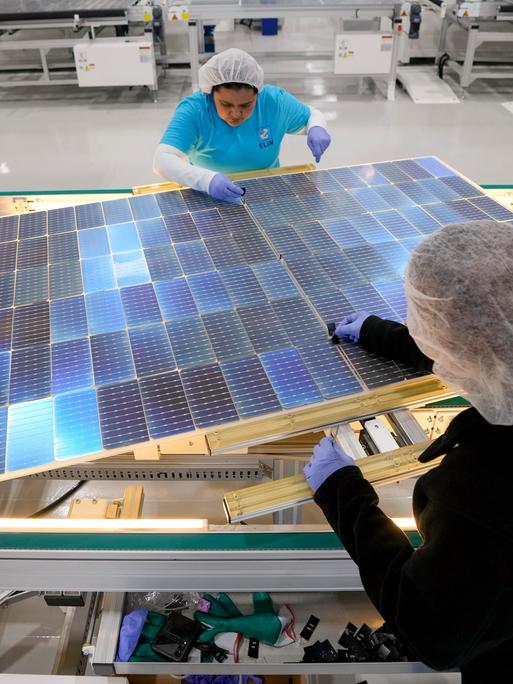 Zwei Frauen arbeiten in einer Fabrik an Solarpaneelen. 