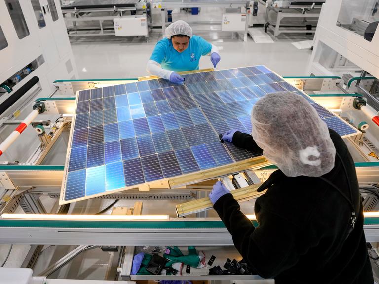 Zwei Frauen arbeiten in einer Fabrik an Solarpaneelen. 