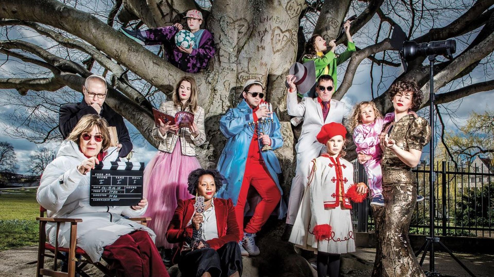 Das Hauptmotiv des 28. Jüdischen Filmfestival Berlin-Brandenburg 2022 zeigt auf dem Festivalplakat mehrere Menschen in bunten Kostümen zusammen unter einem alten Baum.