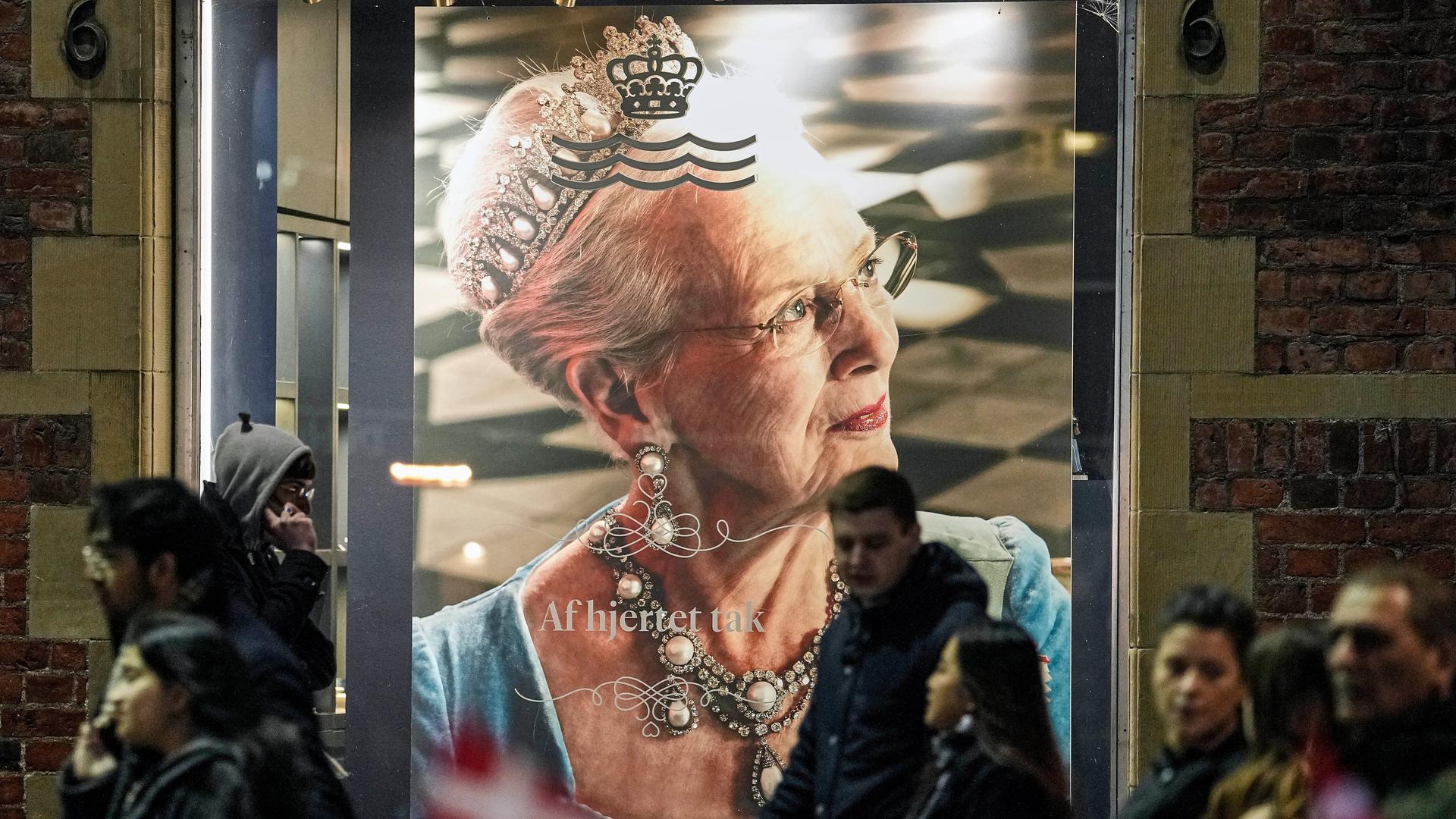Ein großes Porträt der langjährigen dänischen Königin Margrethe II. auf einem Plakat in der Innenstadt von Kopenhagen. Im Vordergrund Menschen, die an dem Plakat vorbeilaufen.