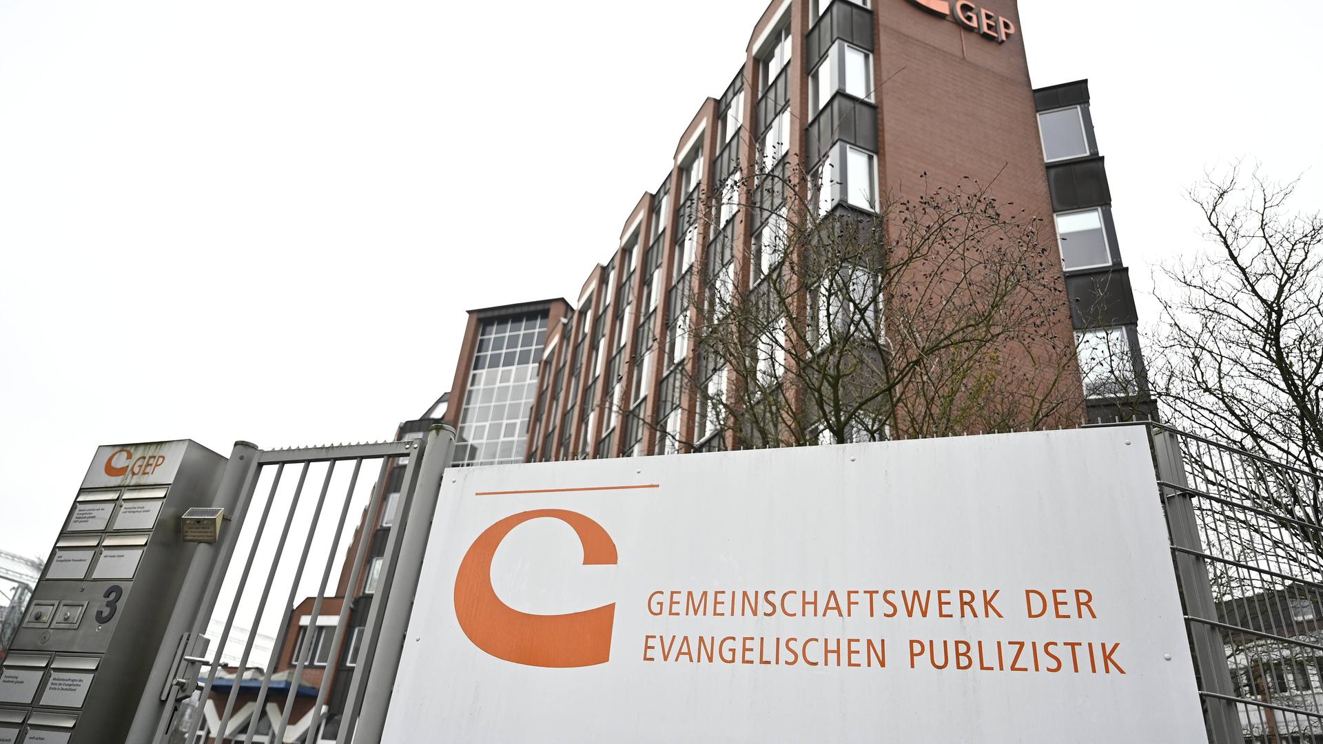 Die Zentrale des Gemeinschaftswerks der Evangelischen Publizistik, ein braunes Gebäude mit einem Schild im Vordergrund.
