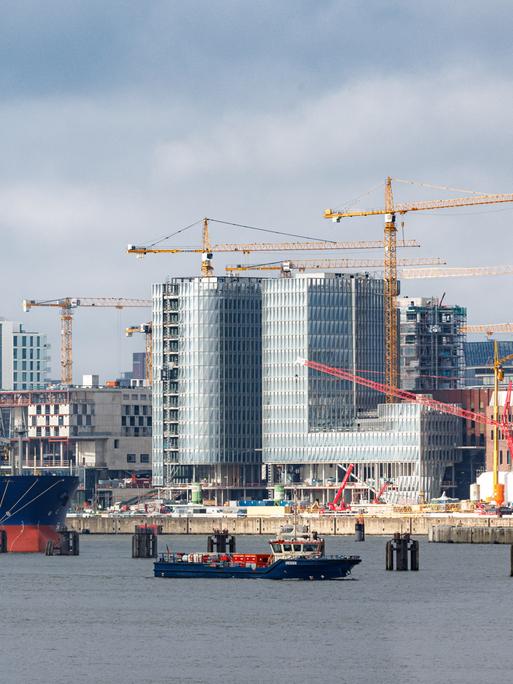 Die Baustelle des Überseequartiers der Hafencity Hamburg am Hafen. Baukräne stehen zwischen fertigestellten und noch unfertigen hohen Gebäuden.