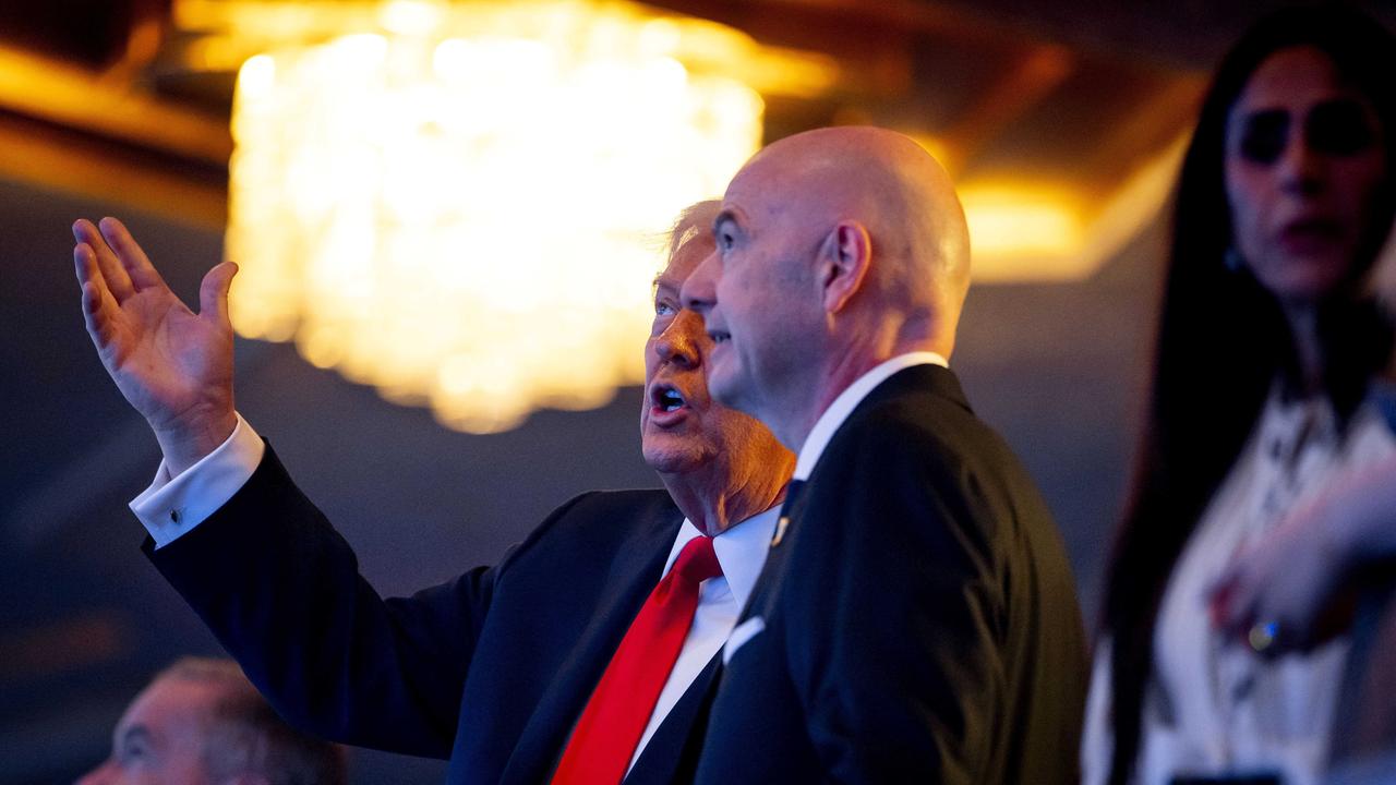 Das Bild zeigt US-Präsident Donald Trump und FIFA-Präsident Gianni Infantino von der Seite. Beide tragen schwarze Anzüge und unterhalten sich. Im Hintergrund ist das Publikum zu sehen.
