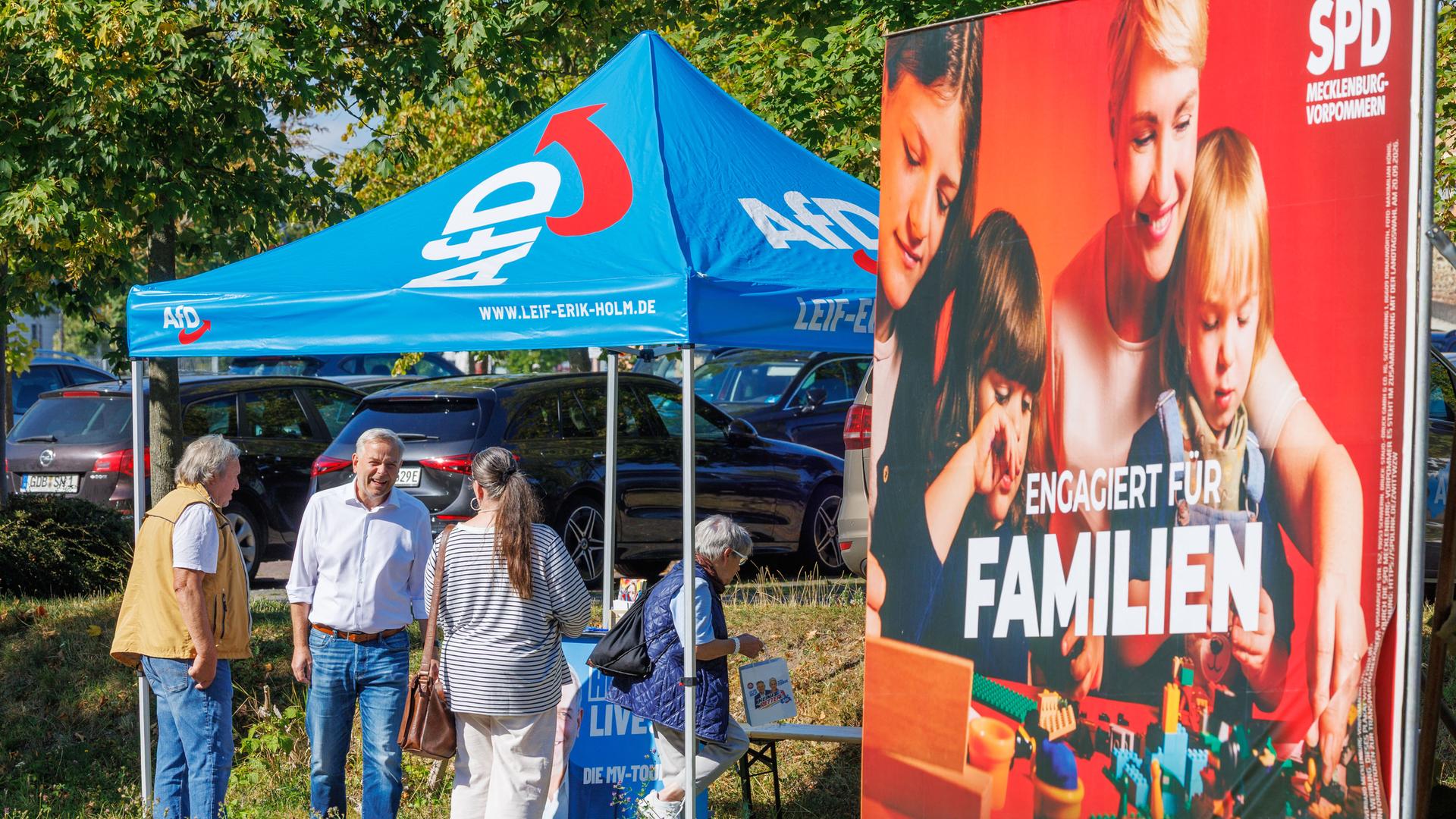 Leif-Erik Holm, AfD-Landesvorsitzender in Mecklenburg-Vorpommern, spricht an einem Informationsstand der Partei mit Passanten. Im Vordergrund ist ein Wahlplakat der SPD zu sehen. Leif-Erik Holm, AfD-Landesvorsitzender in Mecklenburg-Vorpommern, spricht an einem Informationsstand der Partei mit Passanten. Im Vordergrund ist ein Wahlplakat der SPD zu sehen.