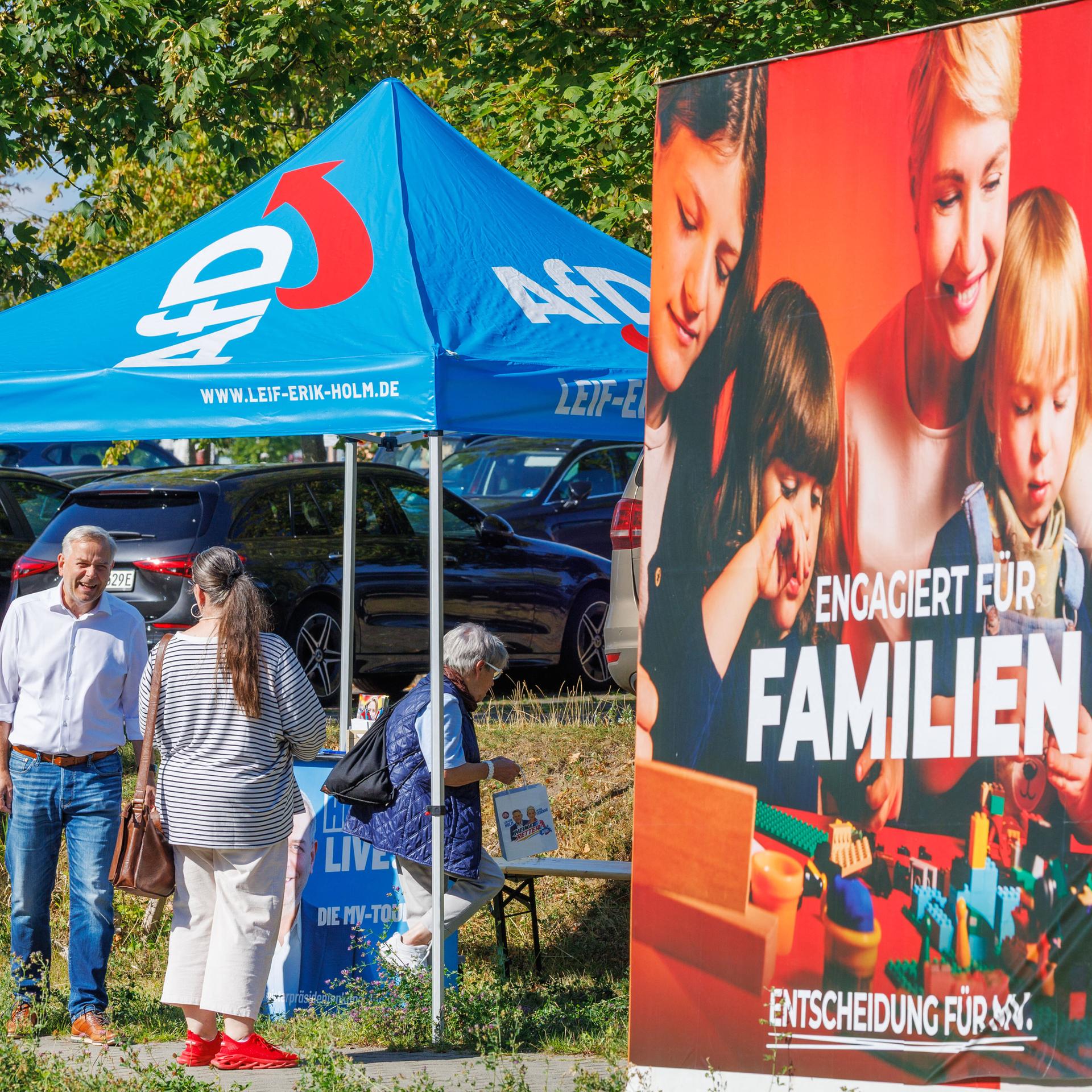 Leif-Erik Holm, AfD-Landesvorsitzender in Mecklenburg-Vorpommern, spricht an einem Informationsstand der Partei mit Passanten. Im Vordergrund ist ein Wahlplakat der SPD zu sehen. 