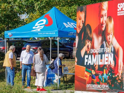 Leif-Erik Holm, AfD-Landesvorsitzender in Mecklenburg-Vorpommern, spricht an einem Informationsstand der Partei mit Passanten. Im Vordergrund ist ein Wahlplakat der SPD zu sehen. Leif-Erik Holm, AfD-Landesvorsitzender in Mecklenburg-Vorpommern, spricht an einem Informationsstand der Partei mit Passanten. Im Vordergrund ist ein Wahlplakat der SPD zu sehen.