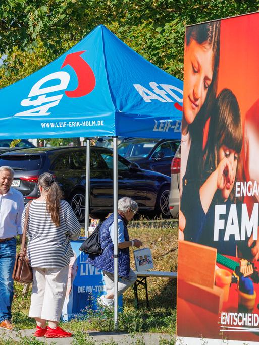 Leif-Erik Holm, AfD-Landesvorsitzender in Mecklenburg-Vorpommern, spricht an einem Informationsstand der Partei mit Passanten. Im Vordergrund ist ein Wahlplakat der SPD zu sehen. 