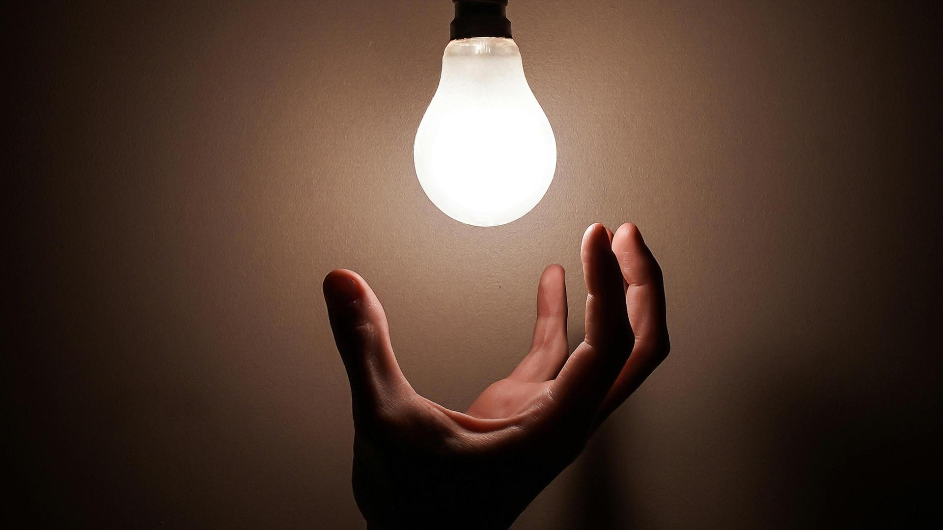Eine Hand greift nach einer Glühbirne.