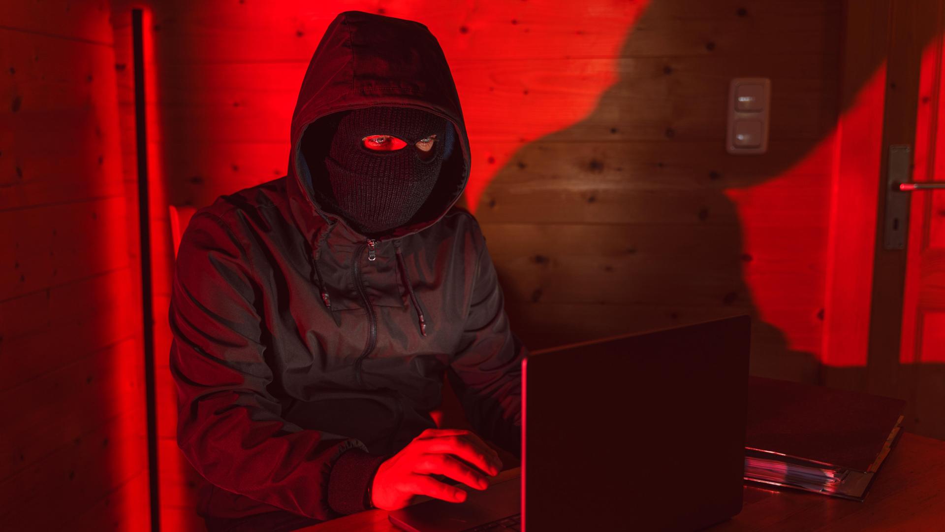 Ein maskierter Mann sitz am Laptop. Neben ihm liegt ein Smarthpone. Ein maskierter Mann sitz am Laptop. Neben ihm liegt ein Smarthpone.
