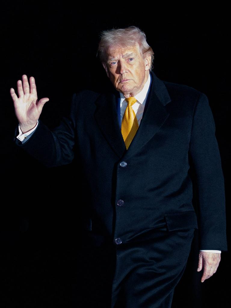 Donald Trump steht im Dunkeln, nur sein Gesicht und die zum Gruß erhobene Hand sind zu sehen